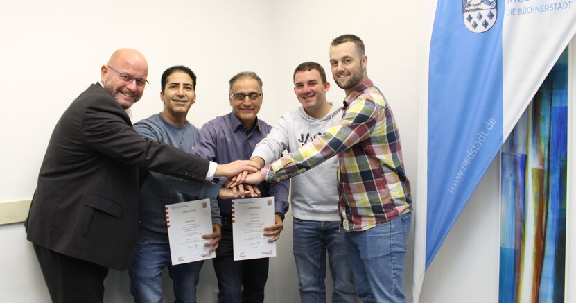 Bürgermeister Marcus Kretschmann, Maher Al Gnem, Samer Chawaf, Tobias Menke und Fachbereichsleiter Rick Hölzer (v.li.) legen ihre Hände übereinander.