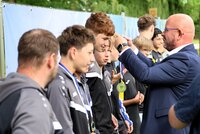 Bürgermeister Marcus Kretschmann zeichnete auch die Fußballer des TSV Goddelau aus. Fußballer des TSV Goddelau stehen in ihren grauen Trainingsanzügen in einer Reihe. Die ersten haben bereits eine Medaille umhängen. Bürgermeister Marcus Kretschmann hängt gerade dem nächsten eine Medaille um.