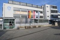 Das Riedstädter Rathaus von außen. Vor dem Gebäude wehen die Deutschlandfahne, die Fahne des Landes Hessen und die der Stadt Riedstadt