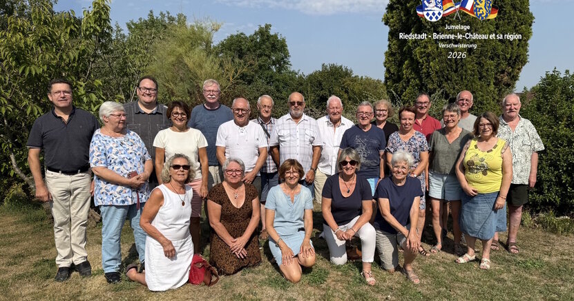 Gastgeber und Gäste stellten sich zum Abschied zu einem gemeinsamen Foto auf. Frauen und Männer aus Riedstadt und Briennel-le-Château haben sich für ein Abschlussbild in zwei Reihen auf einen Rasen gestellt. Im Hintergrund sind Bäume zu sehen.