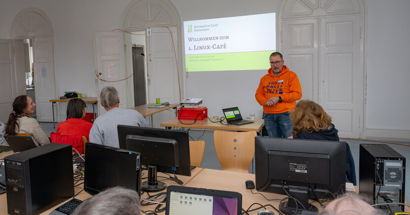 Großen Zuspruch fand auch das zweite Linux-Café in Riedstadt. Vorne steht ein Mann und gibt Erklärungen. Vor ihm sitzen Menschen an Tischen, auf denen Rechner stehen.