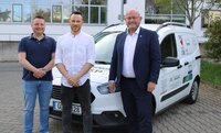 Über das Auto freuen sich Marcus Schramm und Christian Pudel vom IT-Service sowie Bürgermeister Marcus Kretschmann (v.li.) Ein weißes Auto mit verschiedenen Aufschriften steht auf einem Parkplatz hinter dem Riedstädter Rathaus. Auf der Motorhaube ist der Schriftzug "Büchnerstadt Riedstadt" zu erkennen. Vor dem Wagen stehen Marcus Schramm und Christian Pudel von der IT-Abteilung sowie Bürgermeister Marcus Kretschmann