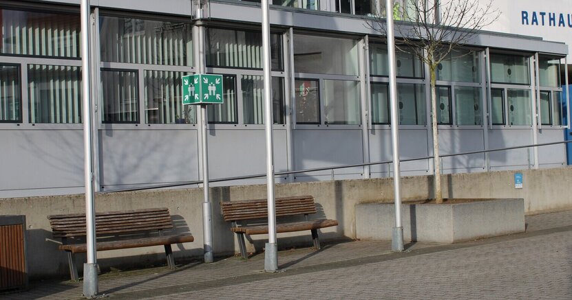Zu sehen ist das Riedstädter Rathaus von außen. Davor stehen zwischen Fahnenmasten zwei Sitzbänke.