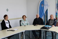 Gleichstellungsbeauftragte Jennifer Muth, Brigitte Lautenbach, Heinz Osterod und Berater Hans-Jürgen Pretzel in einem Raum des Riedstädter Rathauses. Gleichstellungsbeauftragte Jennifer Muth, Brigitte Lautenbach, Heinz Osterod und Berater Hans-Jürgen Pretzel sitzen im Halbrund an einem langen Tisch, im Hintergrund ist die Fahne der Büchnerstadt Riedstadt zu sehen. Sie ist vertikal in eine blaue und eine weiße Seite unterteilt und versehen mit dem Stadtwappen und der Aufschrift in Blau "Büchnerstadt Riedstadt".