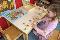 Ein Mädchen sitzt an einem Tisch. Auf dem Tisch liegen Puzzle zum Thema Mülltrennung.