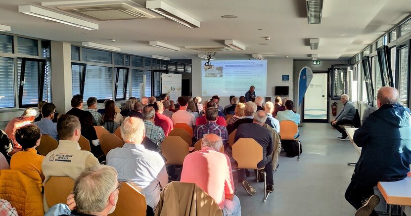 Ein voller Rathaussaal zeigte das große Interesse am Werkstattgespräch über Wärmepumpen. Die vielen Stuhlreihen im großen Sitzungssaal des Riedstädter Rathauses sind voll besetzt mit Menschen, die von hinten zu sehen ist. Ganz vorne ist an der Wand eine Präsentation zu sehen.