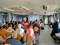 Ein voller Rathaussaal zeigte das große Interesse am Werkstattgespräch über Wärmepumpen. Die vielen Stuhlreihen im großen Sitzungssaal des Riedstädter Rathauses sind voll besetzt mit Menschen, die von hinten zu sehen ist. Ganz vorne ist an der Wand eine Präsentation zu sehen.