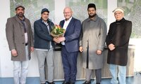 Atta-ul Ghafoor, Abdul Shakoor, Bürgermeister Marcus Kretschmann, Imam Awayes Ahmad Malik und Mumtaz Ahmad (v.li.)stehen im Arbeitszimmer des Bürgermeisters vor Wandbildern, die Luftaufnahmen der Stadtteile zeigen. Der Bürgermeister hat einen Blumenstrauß in der Hand.