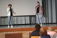 Jessica Davis mit hellblauen Blazer und Kaddy Kupfer mit zerissenen Jeans halten Mikrofone in der Hand und stehen auf der Bühne.
