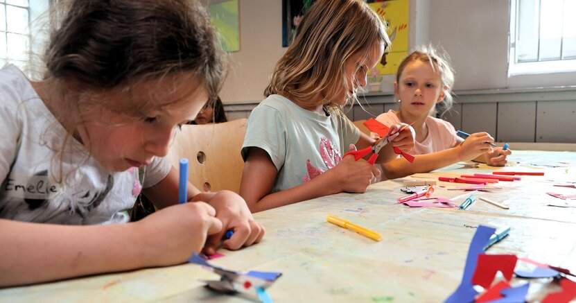 Im letzten Jahr wurden bei den Ferienspielen Leeheim unter anderem Fantasiewesen gebastelt. Drei Mädchen sitzen an einem Tisch, bemalen mit Filzstiften Papier und schneiden etwas aus. Das Foto entstand letztes Jahr bei den Ferienspielen Leeheim