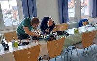 Gemeinschaftlich gewerkelt wird beim Reparatur-Café im alten Rathaus Crumstadt. Zwei Männer beugen sich an einem Tisch über ein elektrisches Gerät. Der eine Mann leuchtet mit einer Taschenlampe, während der andere versucht, das Gerät zu reparieren.
