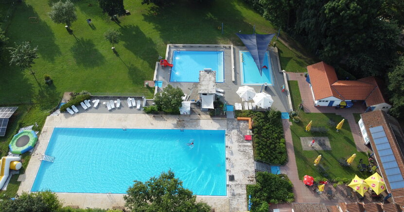 Von oben sind die frei Becken des Freibads Goddelau und die Liegewiesen mit Bäumen zu sehen. Im Vordergrund ist das große Schwimmerbecken mit einem Schwimmer. Dahinter das kleinere Nichtschwimmerbecken und das noch kleinere Planschbecken.