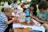 Ferienspielkinder bemalen im Volkspark Goddelau Stirnbänder. Kinder sitzen im Volkspark an einem langen Tisch. Sie bemalen mit bunten Stiften weiße Tuchstreifen.