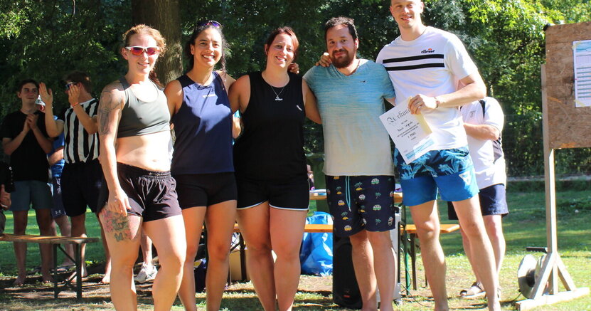 Über den ersten Platz freute sich das Team „Beach Legends“ Drei Frauen und zwei Männer vom Team "Bech Legends" stehen in sommerlicher Sportkleidung auf dem Rasen des Freibads Goddelau. Ein Mann hält die Urkunde für den ersten Platz im Beachvolleyballturnier in der Hand.