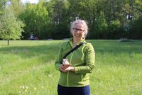 Sandra Wolf, Geschäftsführerin des LPV, steht auf einer Wiese. Im Hintergrund sind Bäume zu sehen. Sie hält einen Gartenschläfer aus Plüsch in ihrer Hand.