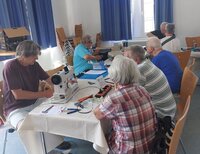 Auch das Reparaturcafé im Alten Rathaus Crumstadt ist Bestandteil der Nachhaltigkeitswoche. Menschen sitzen an langen Tischen im Saal des Alten Rathauses Crumstadt. Auf den Tischen befinden sich Elektro-Geräte, die gerade repariert werden. Im Vordergrund ist eine Nähmaschine zu sehen.