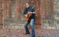 Don Alder steht mit seiner Gitarre vor einer Steinmauer