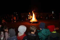 Kinder sitzen auf dem Parkplatz Bürgerhaus um ein großes Feuer herum.