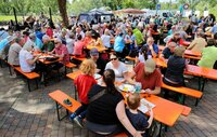 Viele Menschen sitzen beim Ökomarkt auf Bänken, im Hintergrund ist das Gitarrenduo "Love on the Rocks" zu sehen