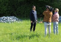 Fachgruppenleiter Holger Schanz steht auf einer Wiese. Vor ihm ein Mann, der eine Kamera auf der Schulter trägt und ihn filmt. Neben dem Mann steht die Redakteurin und stellt Fragen. Im Hintergrund ist einer der Steinhaufen für den Gartenschläfer zu sehen.