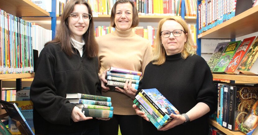 DasTeam der Stadtteilbücherei Goddelau mit Yarisha Garcia Raß, Barbara Niepoth und Sonja Laber (v.li.) steht zwischen Bücherregalen. Alle drei Frauen haben Bücherstapel in der Hand.
